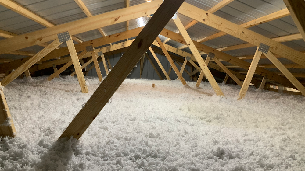 A barn attic completely filled with fresh blown-in insulation between exposed wood roof trusses, completed by Brothers Insulation