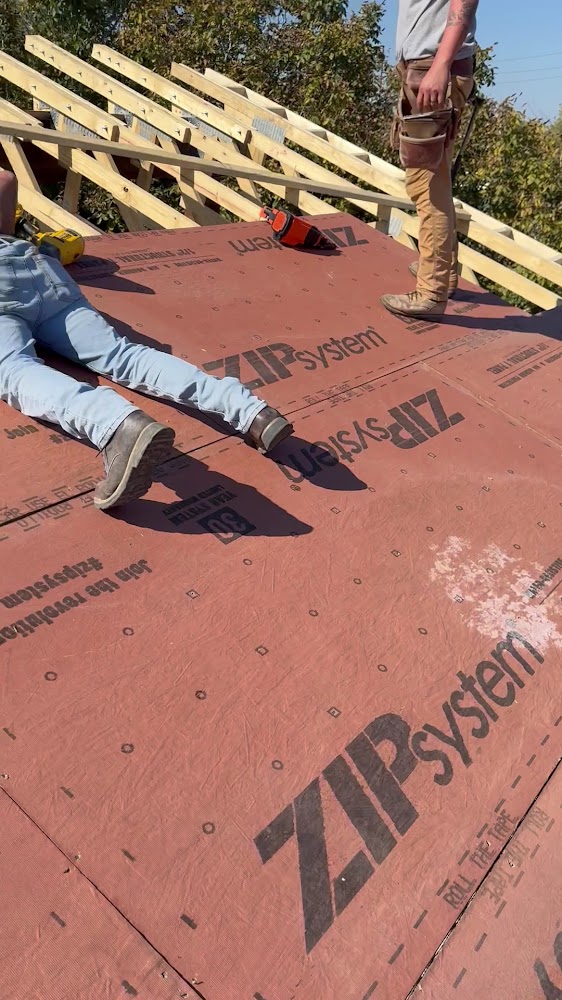 New roof framing and sheathing under construction, with a crew member on the roof deck