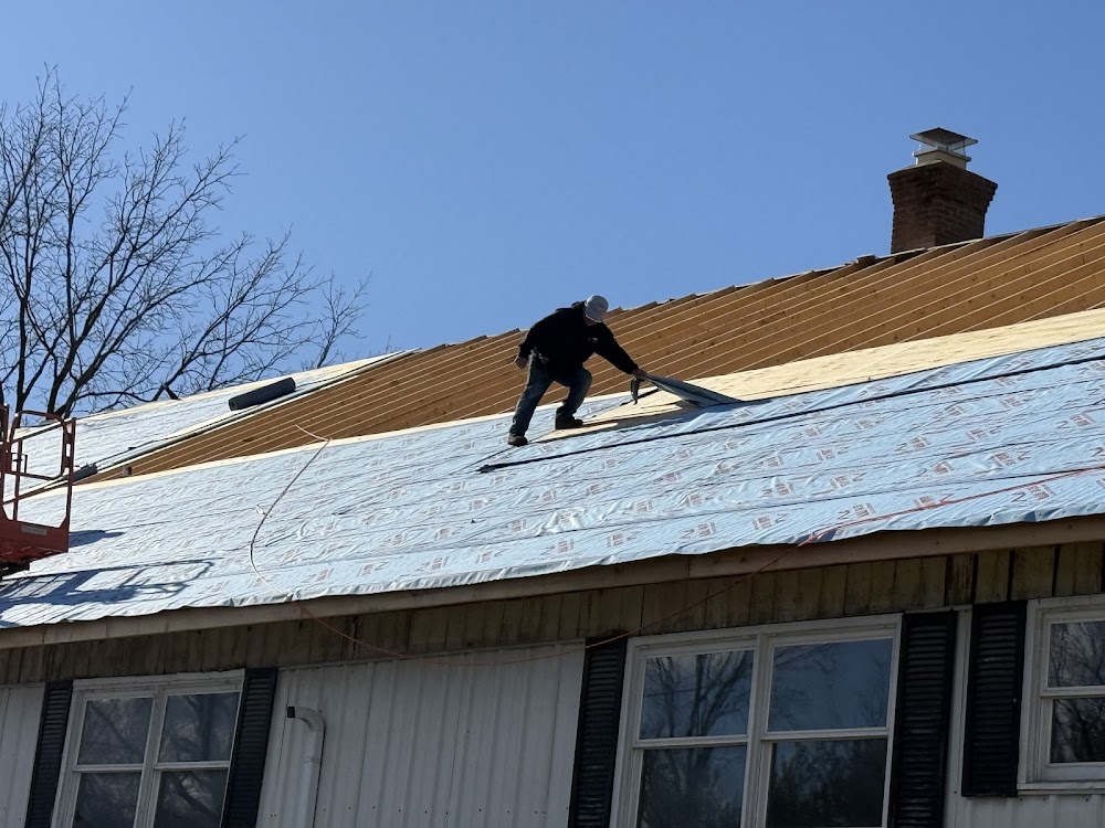 A crew member installing underlayment on a roof, with the chimney and roof deck visible